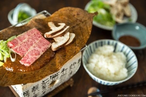 Hida rundvlees met miso op een magnoliablad boven een houtskoolvuurtje, met rijst ernaast
